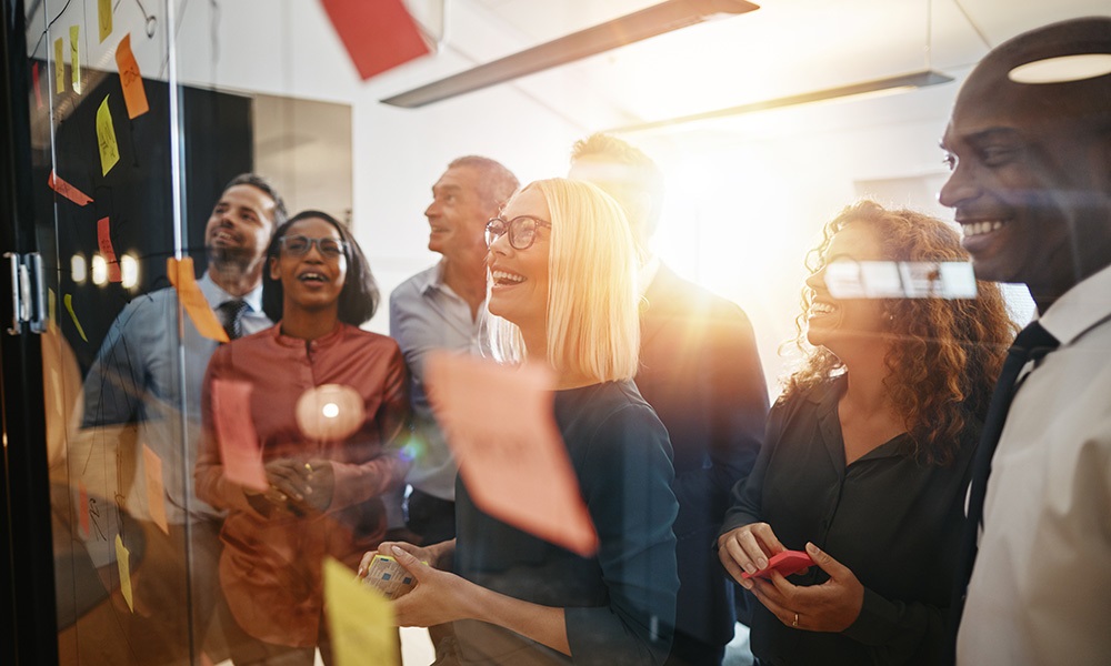 diverse group of people looks enthusiastic at a glass wall with post its on it